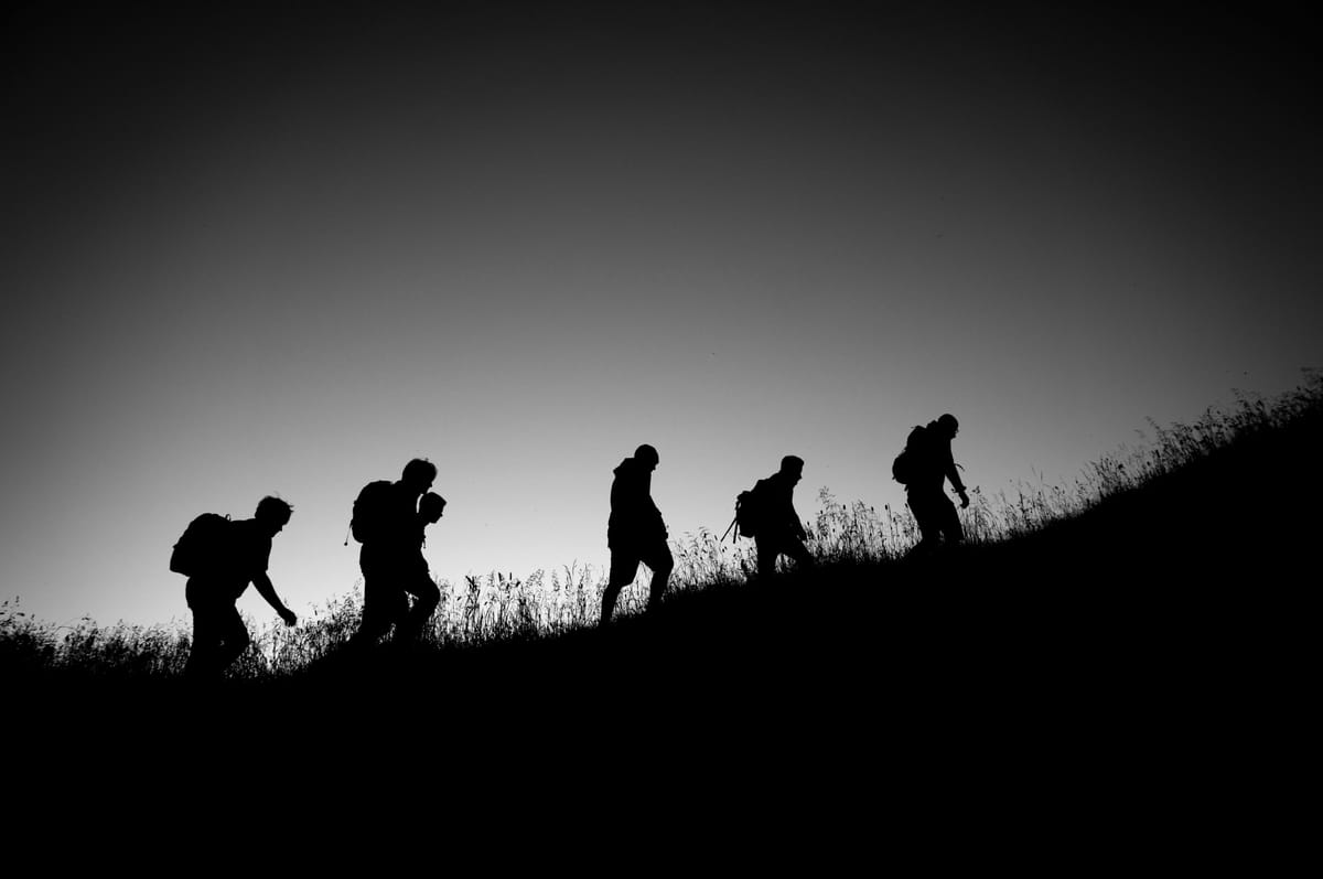 Silhouetted group of hikers walking uphill against a clear sky. The scene evokes a sense of adventure and teamwork in a serene setting.