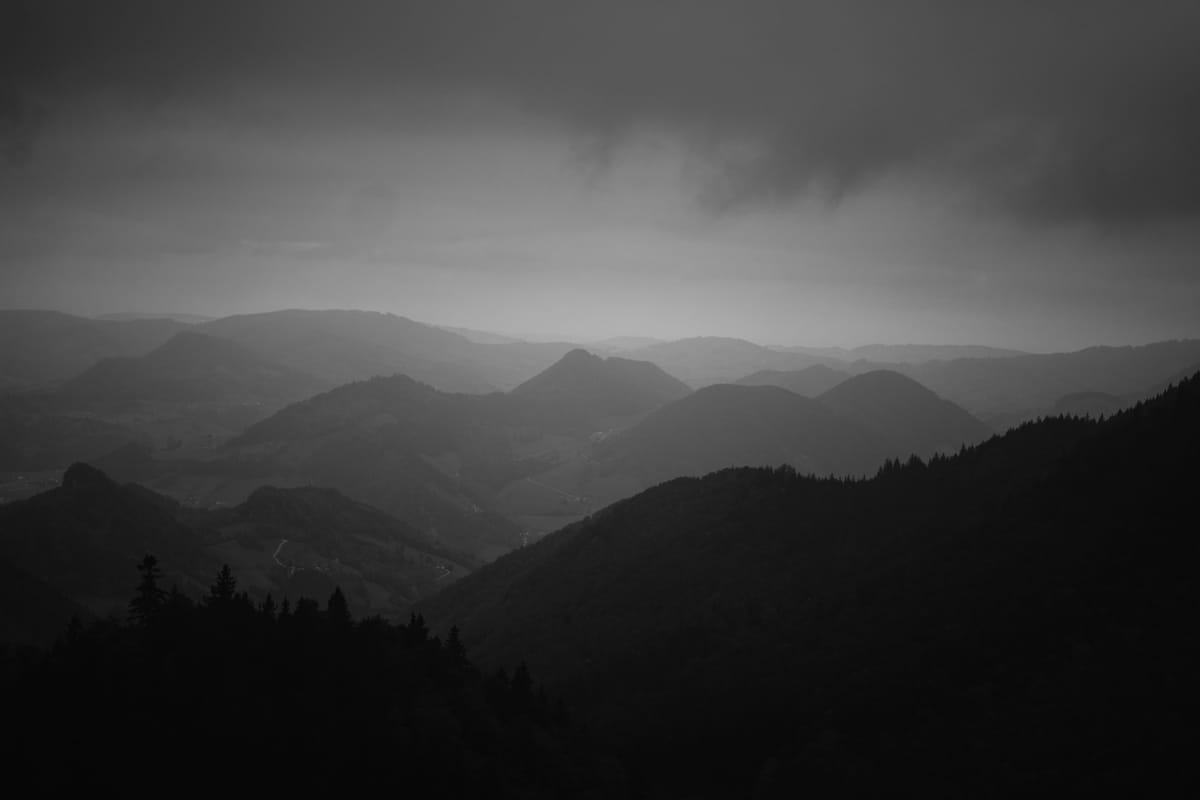 A grayscale panorama of hilly landscapes under an overcast sky. Rolling hills fade into the distance, creating a serene and moody atmosphere.